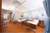 Two hospital-style beds with privacy curtains in a rehab patient room with wood flooring and medical equipment.