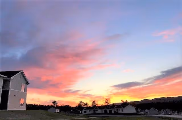 Colorful sunset sky over a residential community with a building on the left and homes along the horizon.