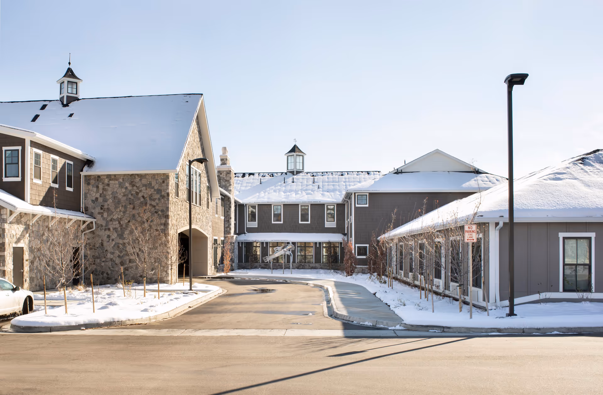 Exterior view of a senior living facility named Balfour Littleton in winter, showing buildings with snow-covered roofs, a driveway, and a few leafless trees along the sidewalk.