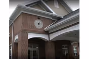 Exterior view of a brick building with a covered entrance featuring white columns and a clock mounted above the entrance.