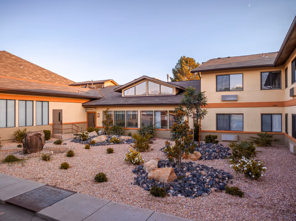 Exterior courtyard of a senior living building with gravel landscaping, rocks, small plants, and a two-story building in the background.