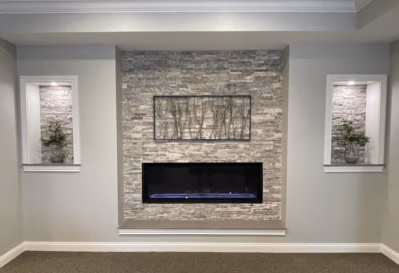 Recessed stone fireplace with a decorative metal wall art above and two lit alcoves containing potted plants.
