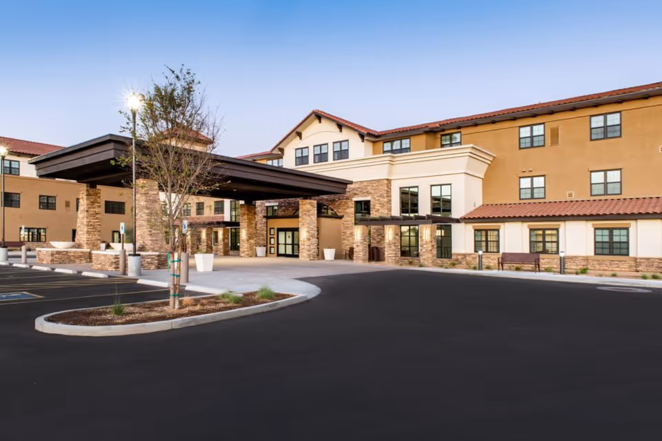 Front entrance of a multi-story senior living facility with a covered porte-cochère and paved parking area.