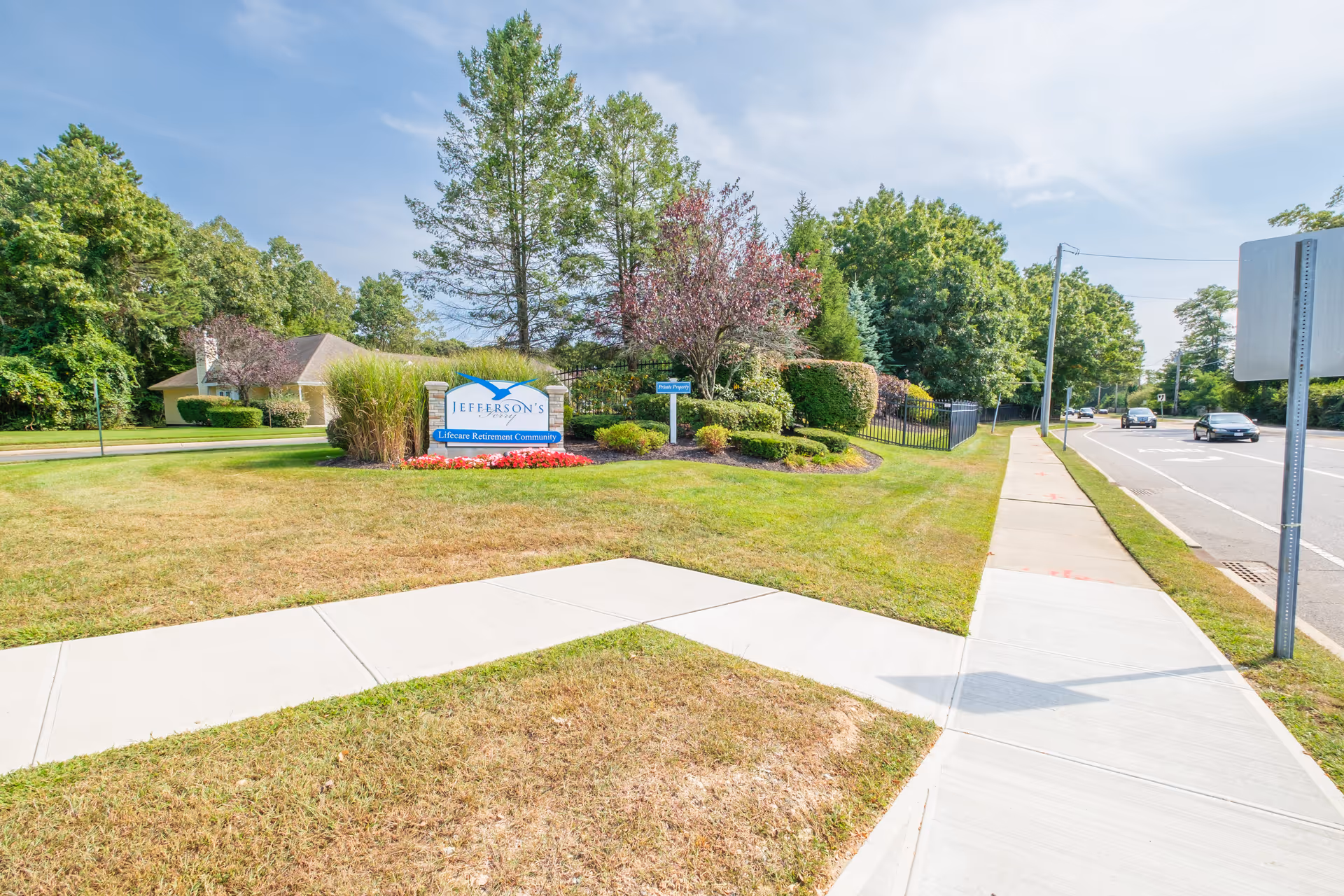 Entrance sign for Jefferson's Ferry surrounded by landscaping next to a sidewalk and road.