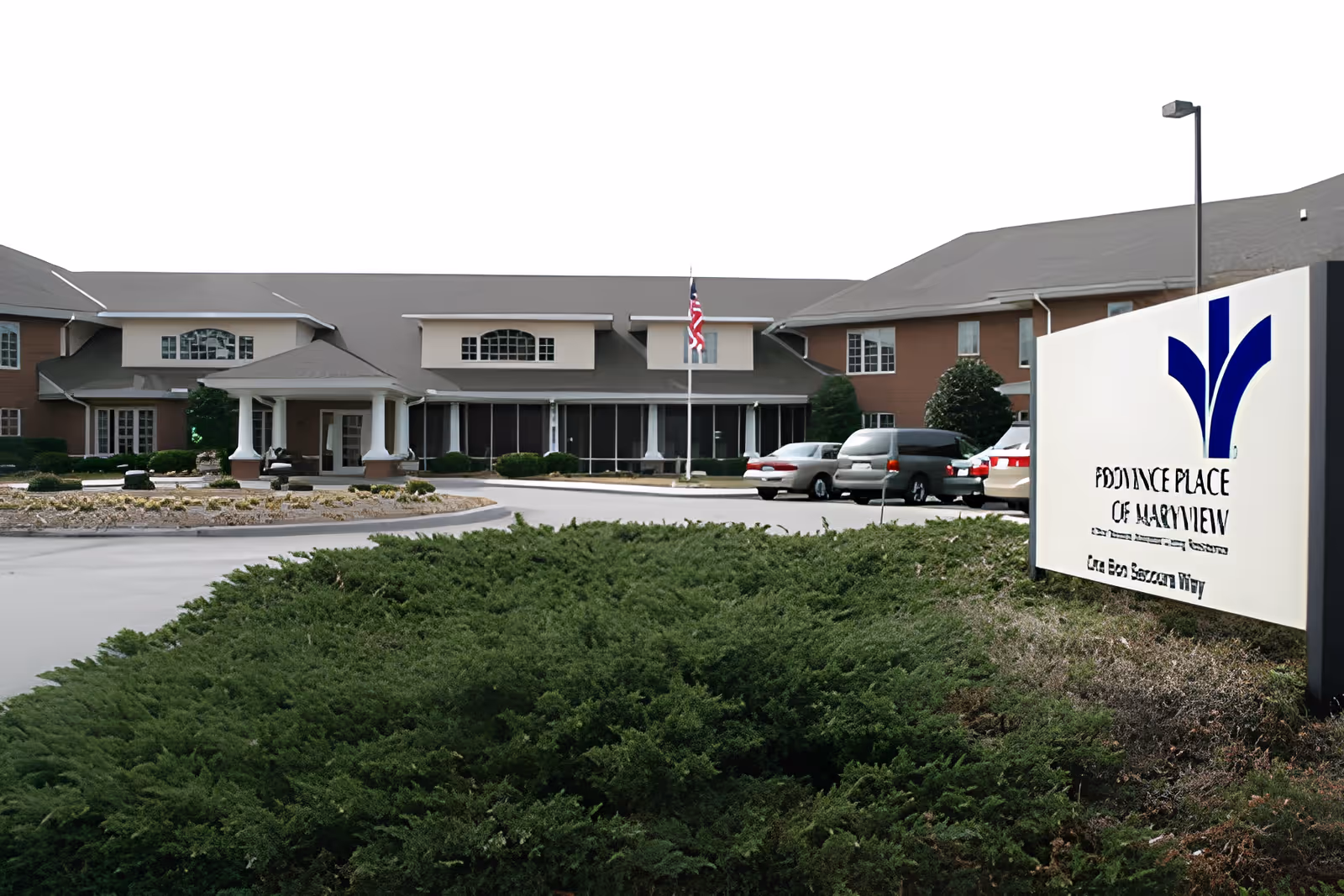 Front exterior of a senior living facility showing the entrance drive, parked cars, an American flag, and a sign reading 'Province Place of Maryview'.