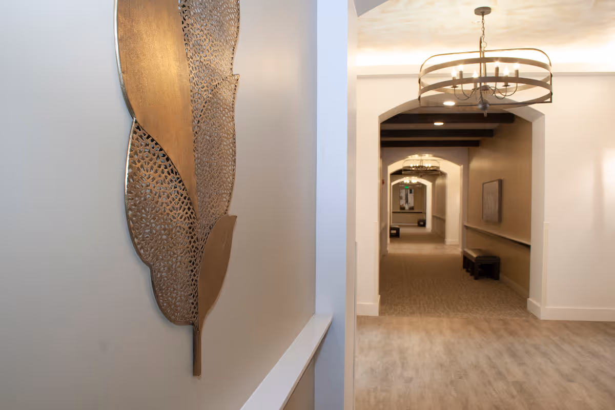 Interior hallway with decorative metal wall art on the left and an arched corridor with chandeliers leading into the distance.