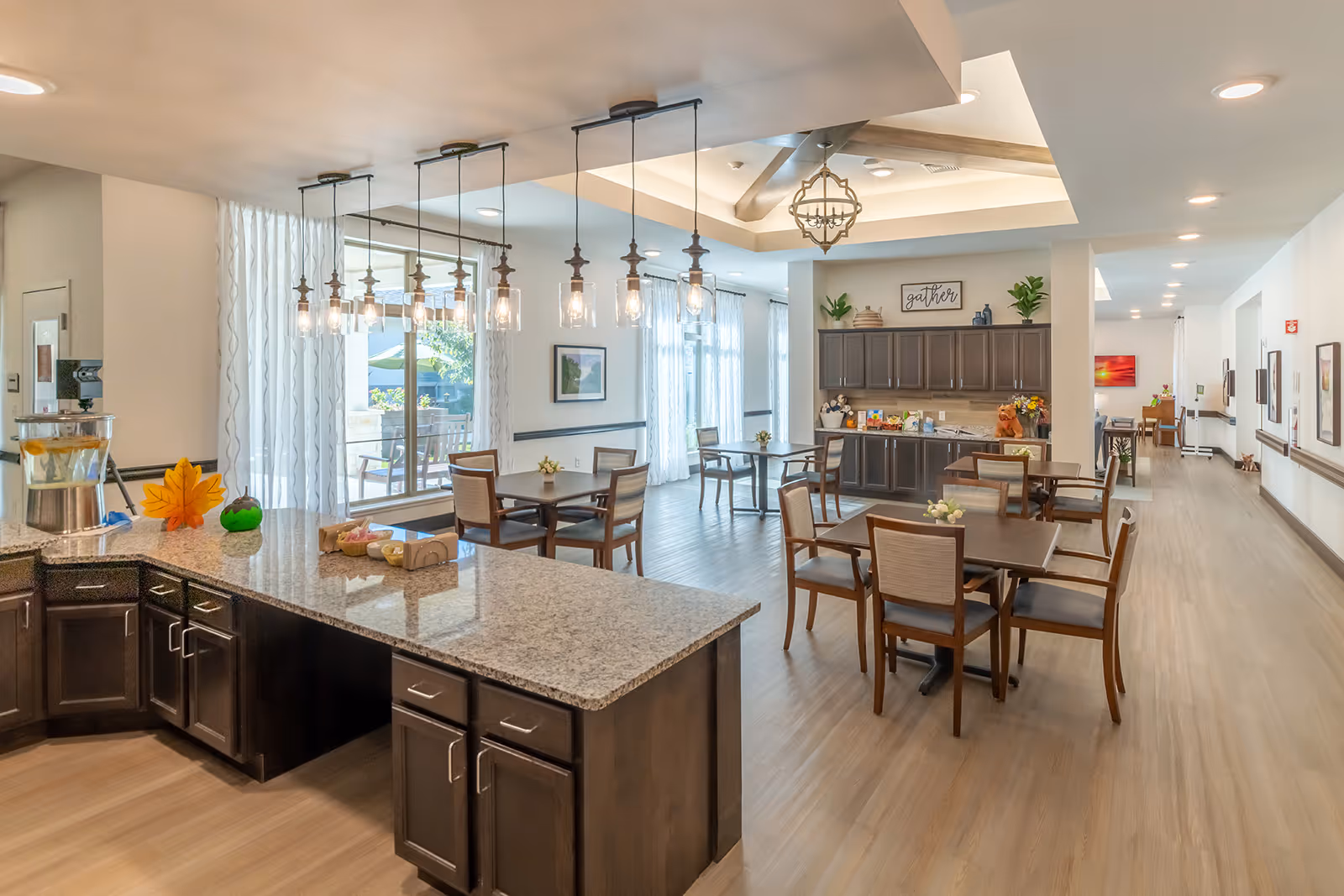 Bright communal dining area and kitchenette with multiple tables, chairs, pendant lights, and a serving counter.