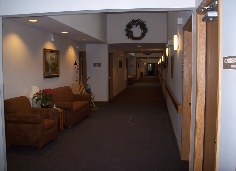 Long interior hallway of an assisted living facility with a seating area, couches, wall art, and overhead lights.