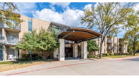 Exterior view of a senior living facility named Autumn Leaves featuring a covered entrance with stone pillars, surrounded by trees and shrubs under a partly cloudy sky.