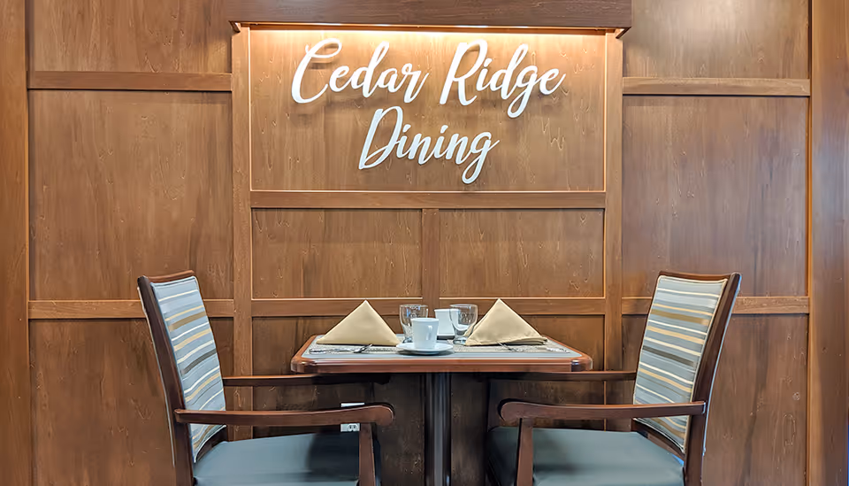 Two-place dining table set with napkins and cups in front of a wood-paneled wall reading 'Cedar Ridge Dining'.