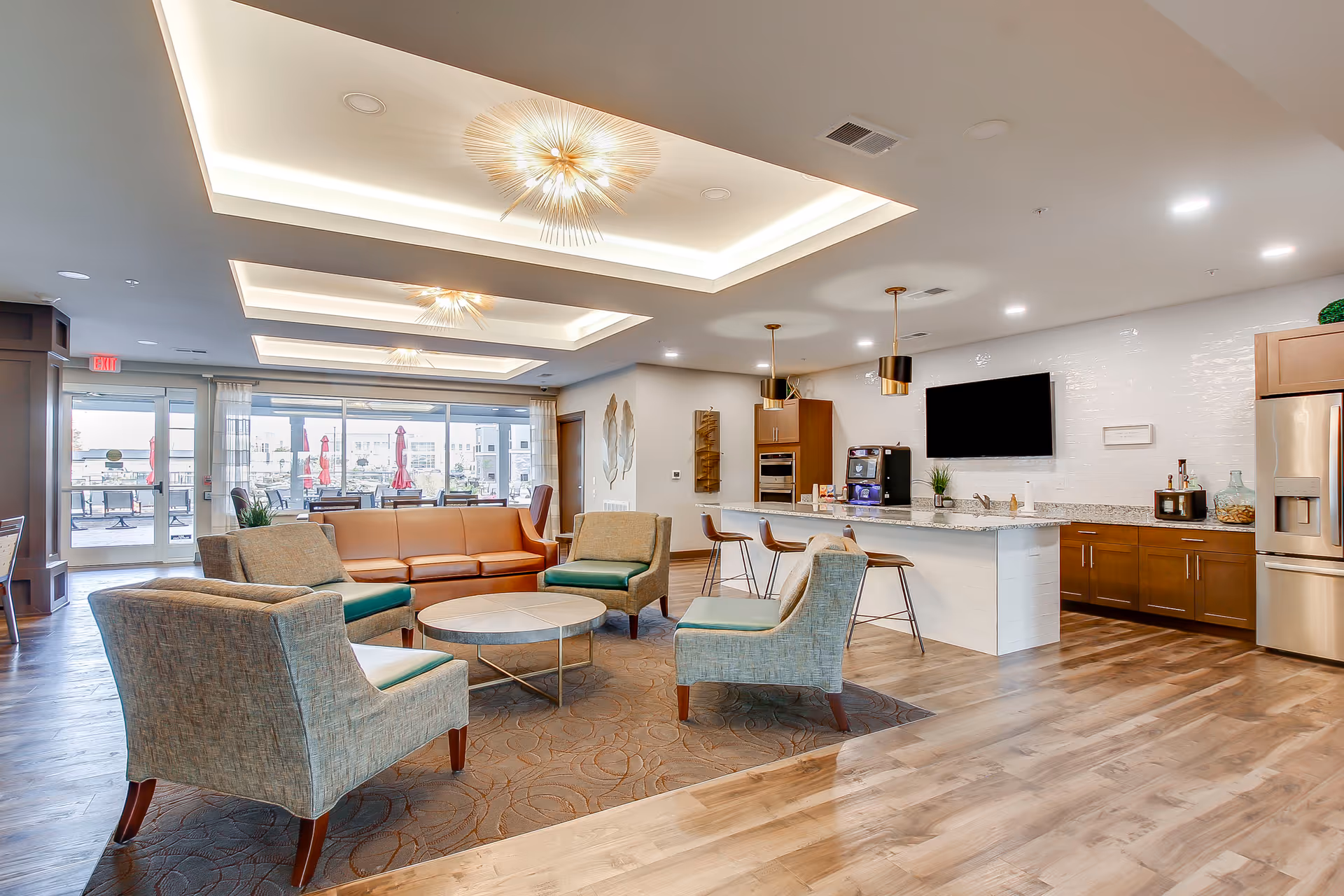 Modern open lounge and kitchenette with seating area, island with bar stools, and large windows opening to an outdoor patio.