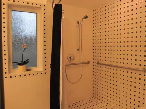 Tiled bathroom with a shower, grab bar, and frosted window.