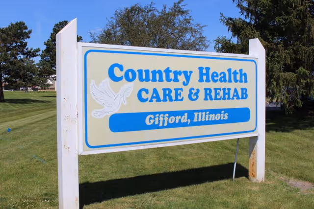 A roadside sign reading "Country Health CARE & REHAB — Gifford, Illinois" on a grassy lawn with trees in the background.