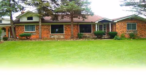 Front view of Jean's Lakeside View: single-story brick facility with lawn and trees.