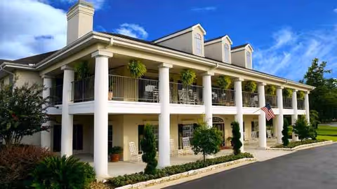 Exterior view of a white, columned senior living facility with a balcony