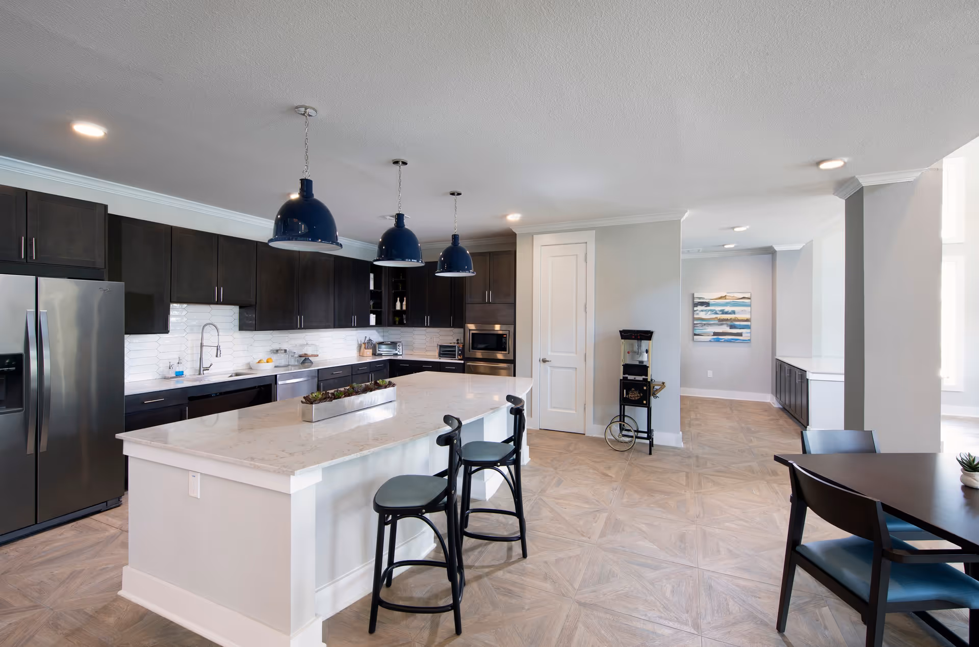 Open modern kitchen with a large white island, three blue pendant lights, dark cabinets, stainless steel appliances, and bar seating.
