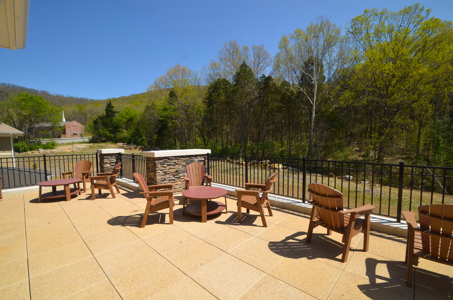 Outdoor terrace with wooden chairs and tables overlooking a wooded landscape.