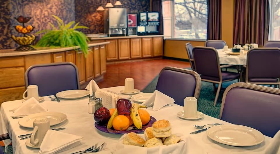 Dining room with neatly set tables, a plate of fruit and biscuits, and a beverage station in the background.