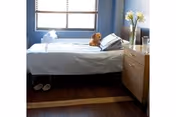 Neatly made bedroom with bed, dresser, window, slippers, and a teddy bear.