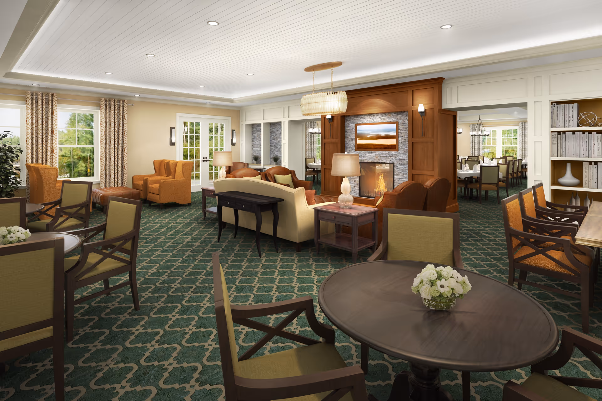 A spacious and well-lit living room area in a senior living facility with green patterned carpet, multiple seating arrangements including armchairs and sofas, a fireplace with a mounted TV above it, and large windows with curtains allowing natural light to enter. There is a dining area visible in the background through an open doorway.