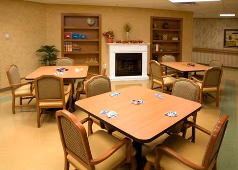 Interior dining room in a senior living facility with tables, chairs, and a fireplace.