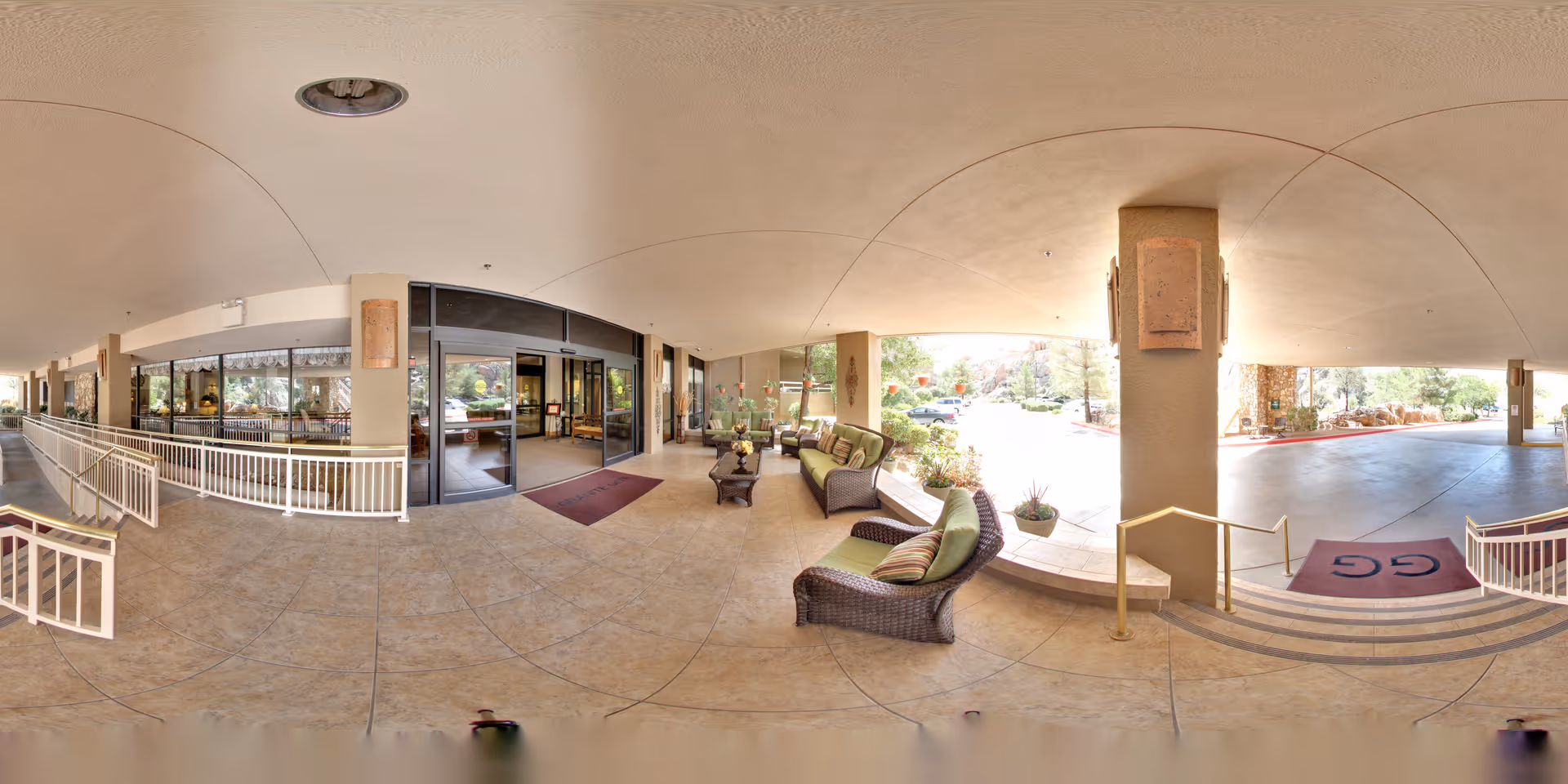 Covered front entrance and drop-off area with wicker seating, potted plants, and sliding glass doors into the senior living lobby.