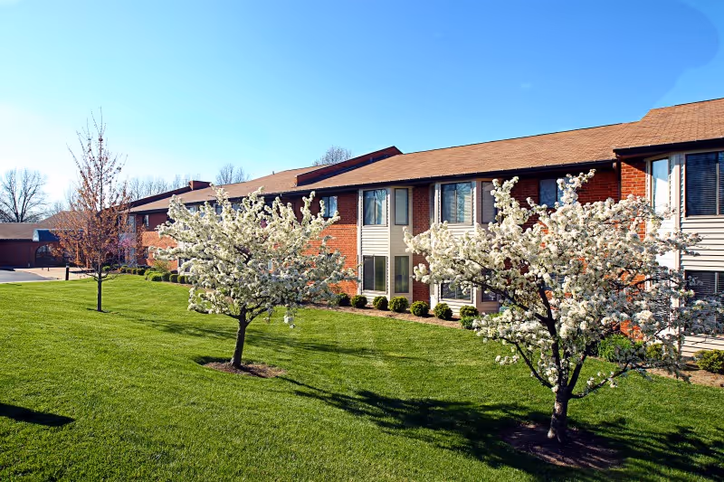 Two-story brick building with blooming trees and a manicured lawn under a clear blue sky.
