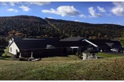 Exterior of Mrs Bushs Personal Care Homes: single-story building with a dark roof, lawn, hills.