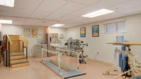 Interior rehabilitation gym with parallel bars, exercise machines, and a stair-climbing setup.