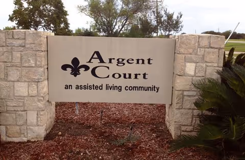 Stone sign for Argent Court, an assisted living community, set between two stone pillars with some greenery and trees in the background.