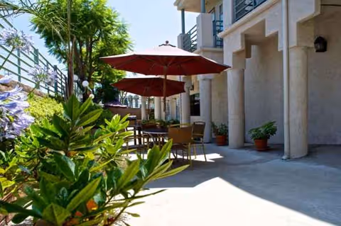 Outdoor patio at Whitten Heights with tables, red umbrellas, and potted plants.