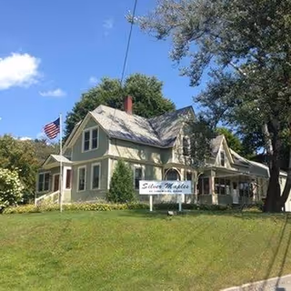 Front view of a two-story pastel senior living home with a sign and flag.