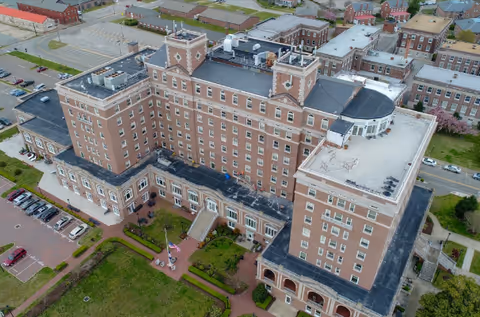 Aerial view of a large multi-story red-brick senior living building with landscaped grounds and a flagpole in front.