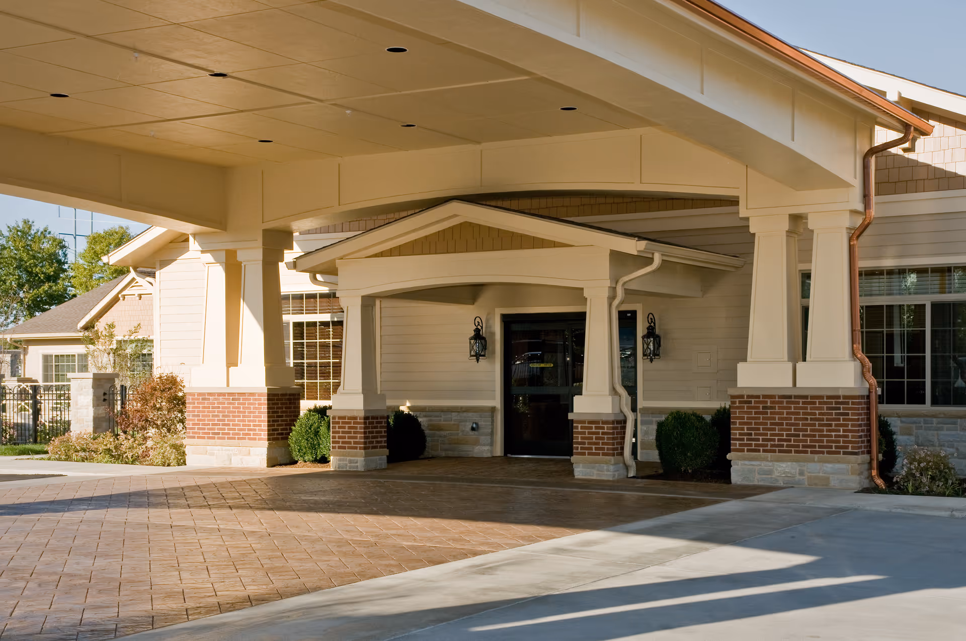 Covered entrance and porte-cochere of a senior living facility with columns, brick accents, and a paved driveway.