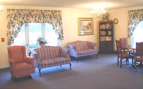 Cozy common living room with striped sofas, armchairs, a bookshelf, and floral curtains.