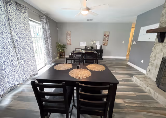 Interior dining room with dark wood tables, chairs, placemats, a potted plant, and a fireplace.
