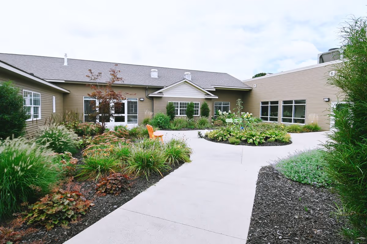 Paved courtyard with landscaped garden beds, seating, and surrounding single-story beige building.