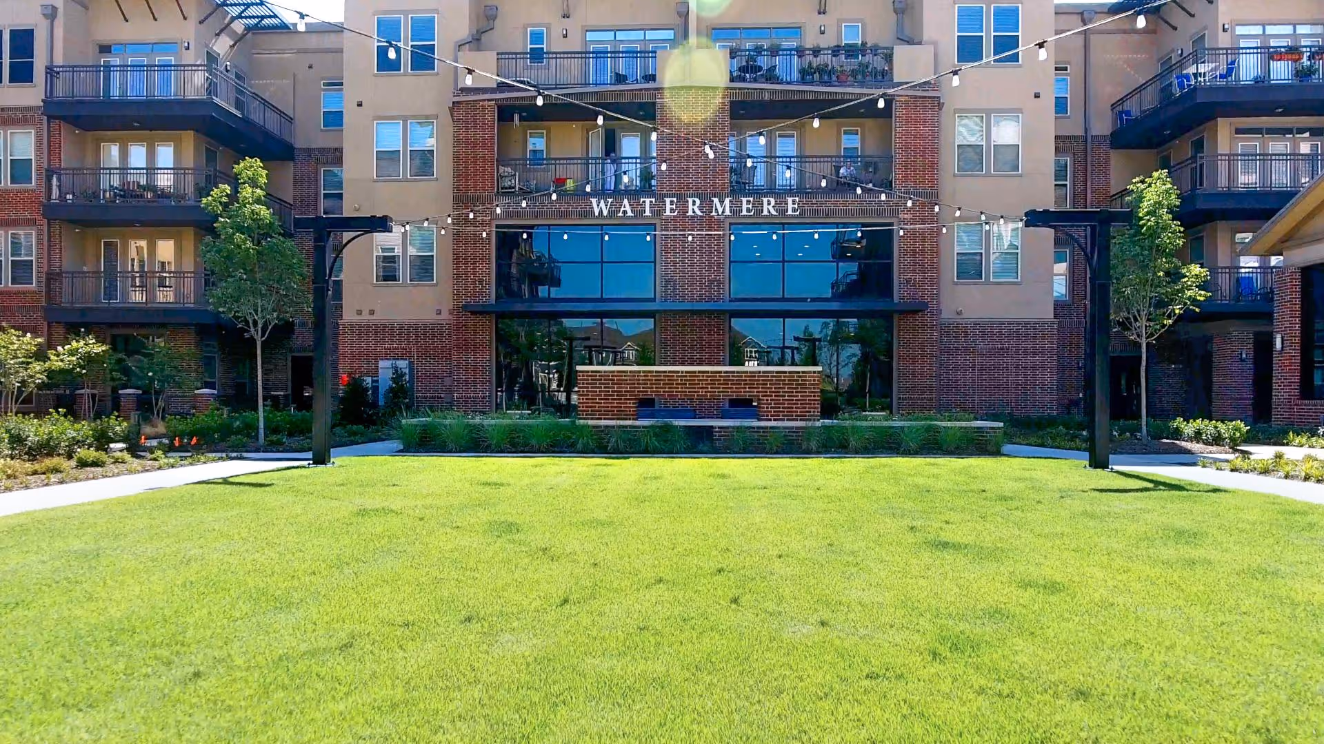 Outdoor view of Watermere at Frisco building with a well-maintained green lawn in the foreground, string lights hanging above, and balconies on the building's facade.