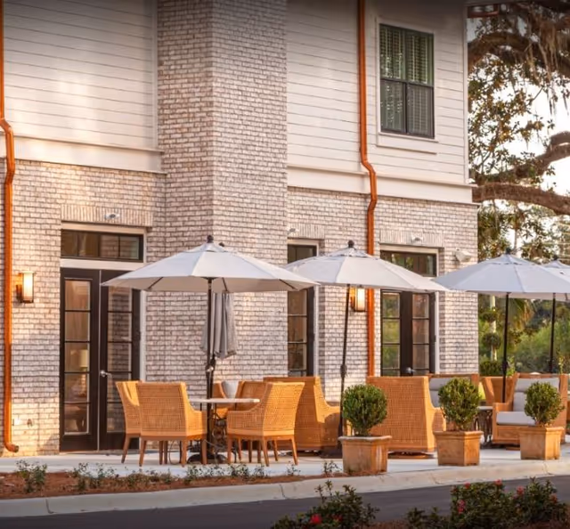 Outdoor patio with wicker chairs, tables and umbrellas arranged outside a light-brick building.