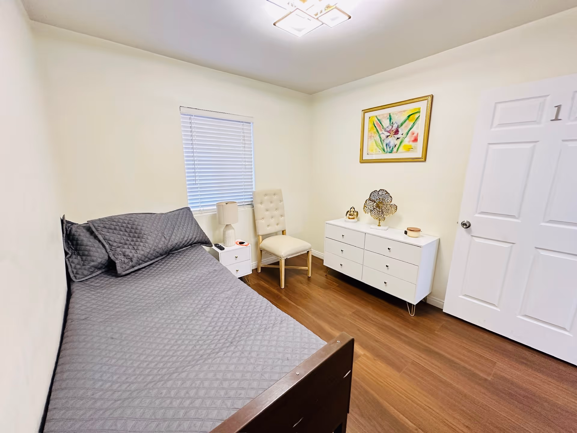 Small bedroom with a single bed, dresser, chair, and colorful wall art.