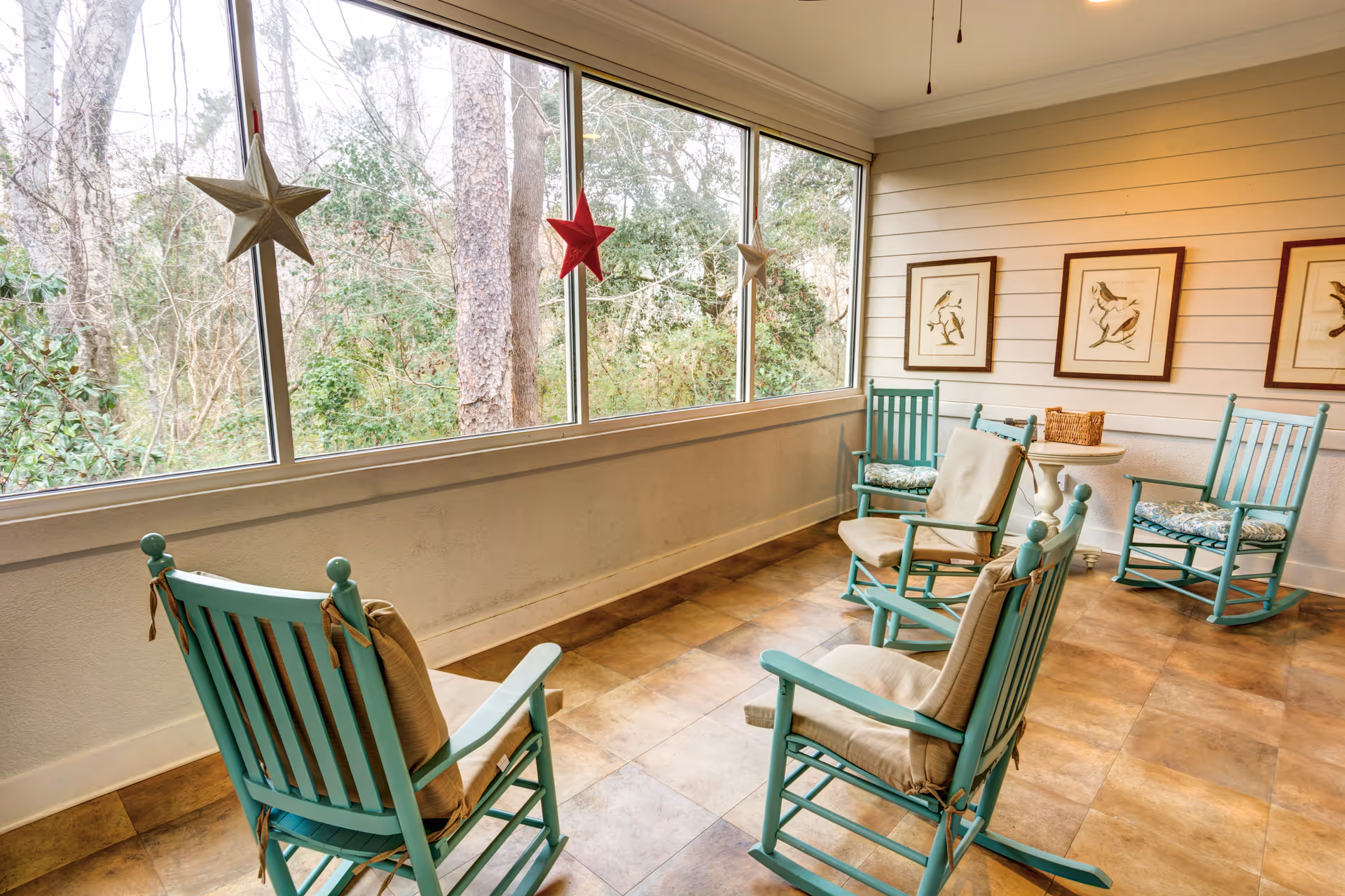 Sun-filled sitting room with turquoise rocking chairs arranged by large windows overlooking trees.
