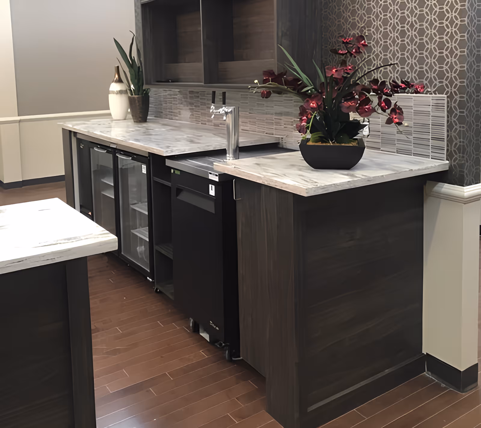 Modern kitchenette/bar area with marble countertops, under-counter refrigerators, a faucet, and decorative plants.