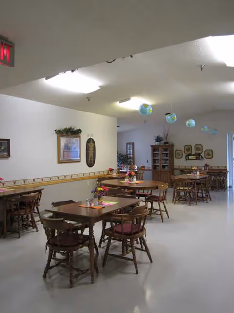 Spacious Birchwood Apartments dining hall with wooden tables, chairs, hanging globes, and wall art.