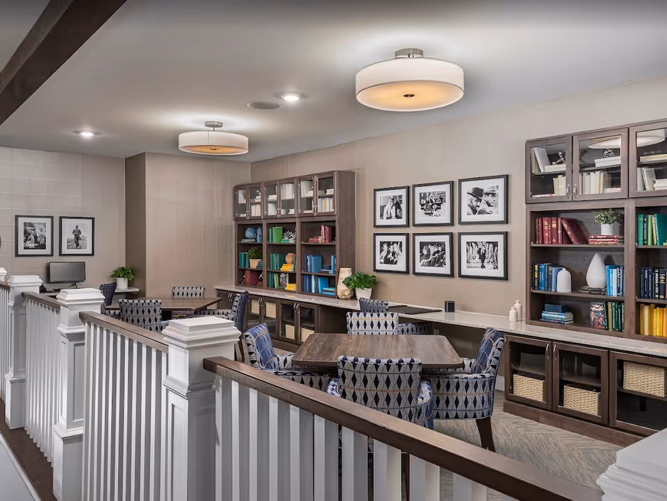 Community lounge with tables, patterned chairs, built-in bookshelves and framed black-and-white photos on the wall.
