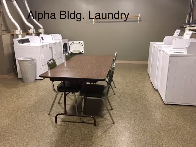 Laundry room with washers and dryers along the walls and a folding table with chairs in the center.