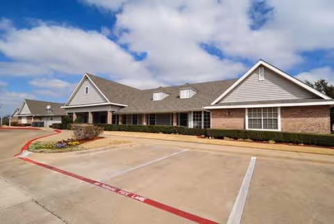 Single-story brick senior living facility exterior with a parking lot and trimmed landscaping.