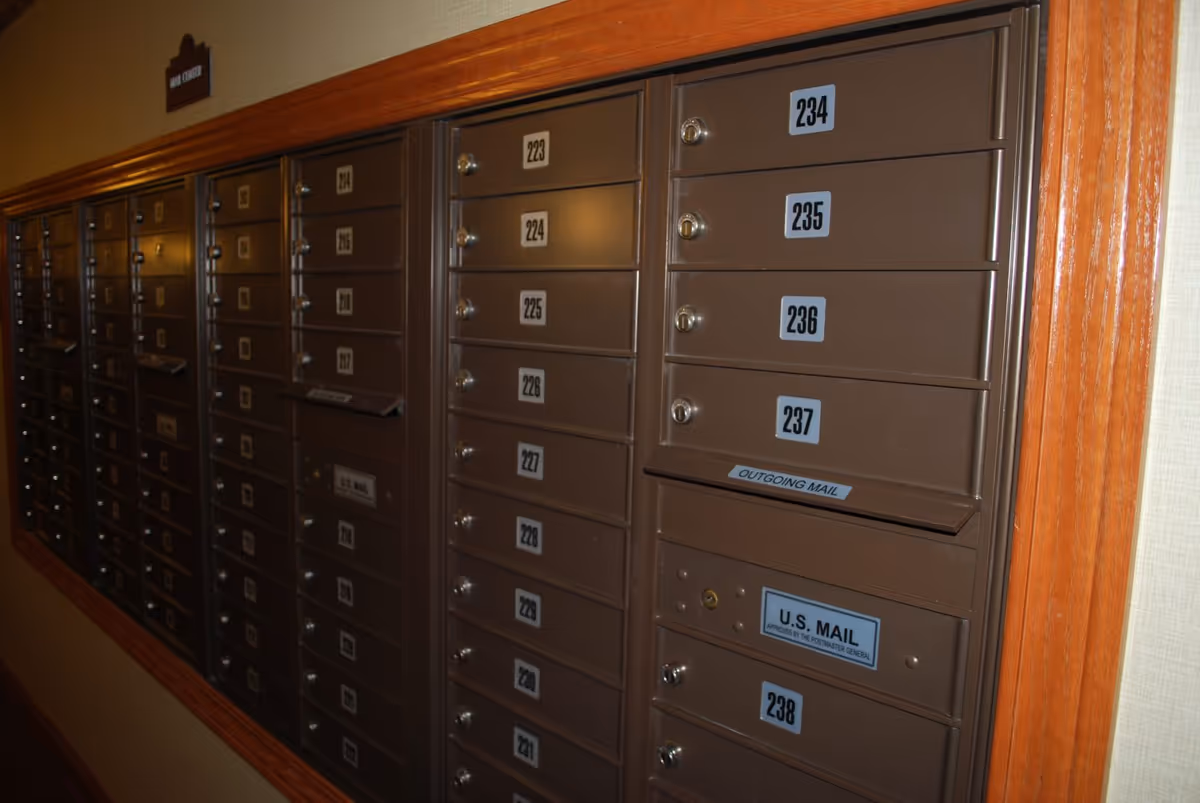 A row of numbered brown mailboxes with an outgoing mail slot mounted in an interior hallway wall.