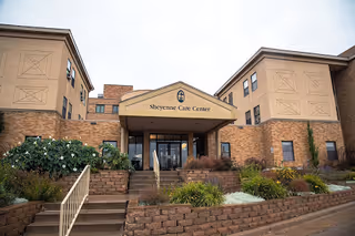 Front entrance of the Sheyenne Care Center, a brick multi-story building with steps and landscaped planters.