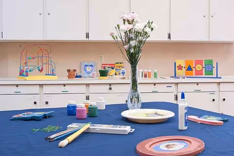 A craft room interior with art supplies on a blue table and vase of flowers.