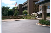 Exterior view of a multi-story brick building with an American flag on a flagpole, landscaped greenery, and a covered entrance driveway at the Jewish Healthcare Center.